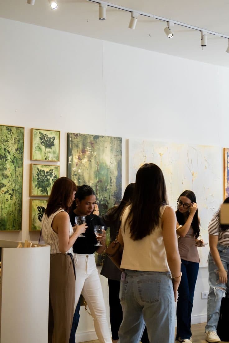 Guests viewing artwork with drinks in hand at a gallery opening.